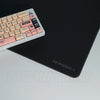 A white mechanical keyboard is placed on a black gaming mouse pad desk mat.