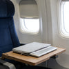 A laptop sleeve is placed on a tray table in an airplane seat, next to a window.