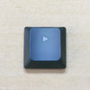 A close-up view of a dark blue replacement keycap with a white triangle marker on a light surface.