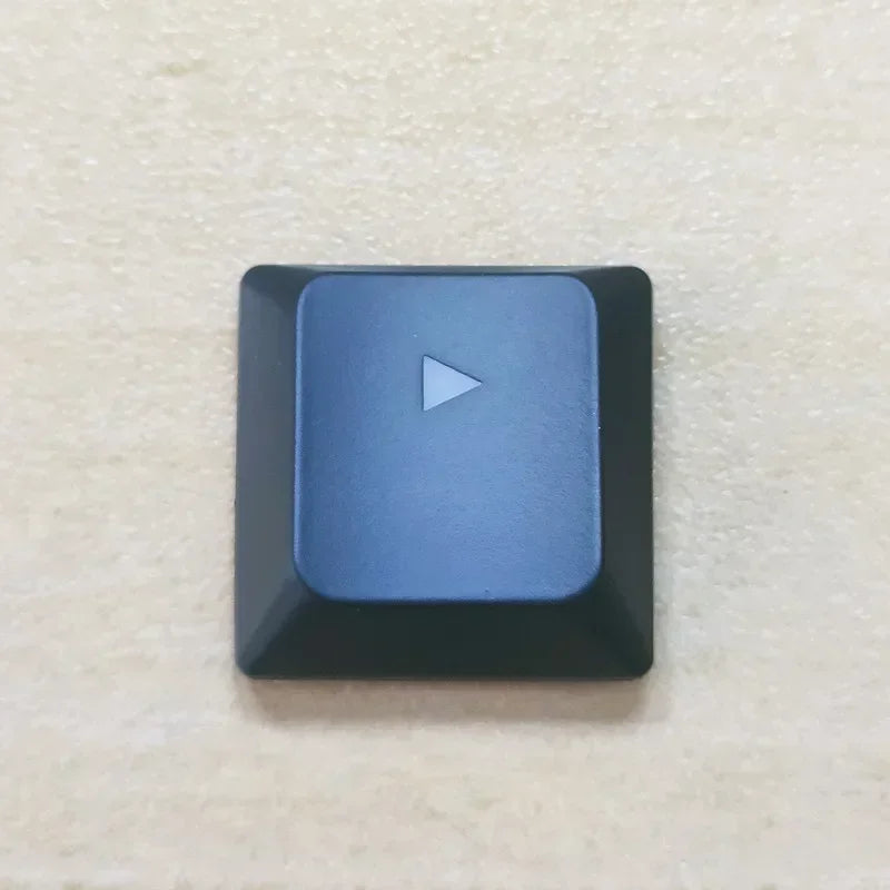 A close-up view of a dark blue replacement keycap with a white triangle marker on a light surface.