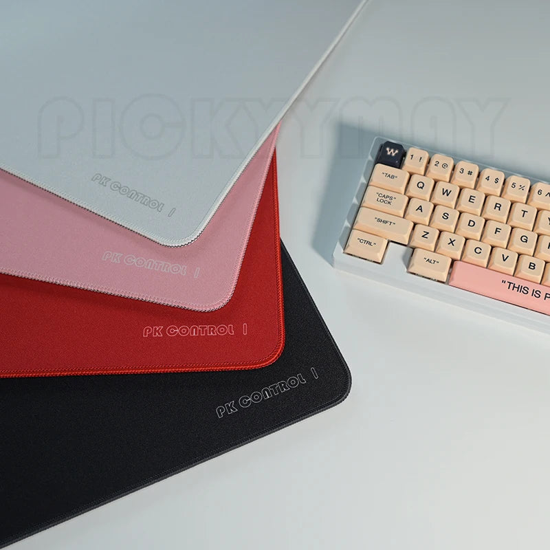 A set of three pink, red, and black professional gaming mouse pads are displayed on a white desk surface.