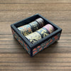 A set of metallic gold washi tape rolls displayed inside a dark wooden box.