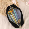 A black zippered pencil case filled with various colored pens and pencils rests on a beige fabric next to a woven mat.