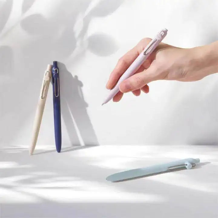 A hand holds a pink precision gel pen with quick-drying ink against a bright white background.