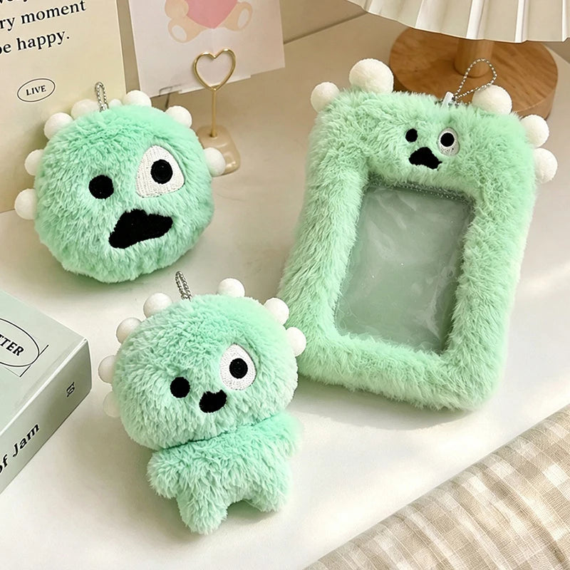 A set of soft green plush toys shaped like monsters with clear window holders on a white surface.