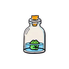 An enamel pin featuring a green frog swimming in a glass bottle with an orange stopper.