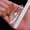 A compact fixed blade knife with a silver blade and gold accents is shown next to a ruler on a hand.