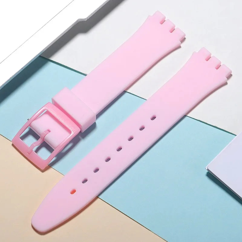 A pink silicone watch strap is shown lying on a light blue background with replacement tools.