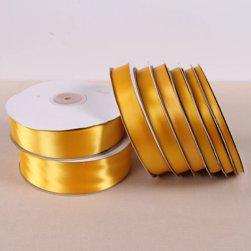 Rolls of gold yellow satin ribbon stacked and laid out on a light surface.