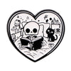 A black enamel lapel pin shaped like a heart featuring a skull, a cat, and an open book.