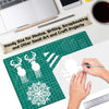 A hand is using a pen on a green cutting mat with a snowflake design for crafting and art projects.