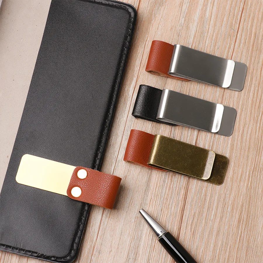A black leather journal is shown with several brass and silver pen holders and clips on a wooden surface.