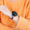 A wrist wearing a black smartwatch with a colorful nylon strap against an orange knitted sweater.