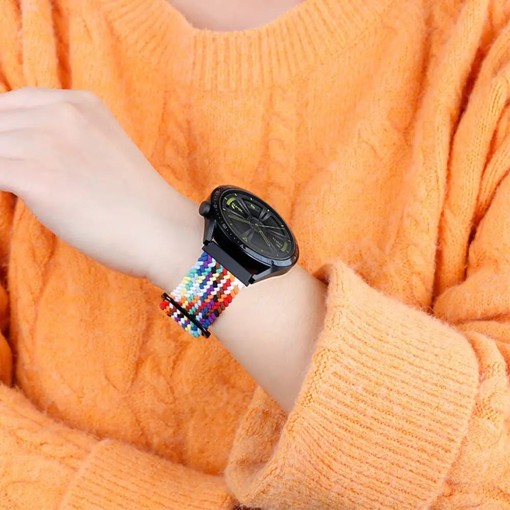 A wrist wearing a black smartwatch with a colorful nylon strap against an orange knitted sweater.