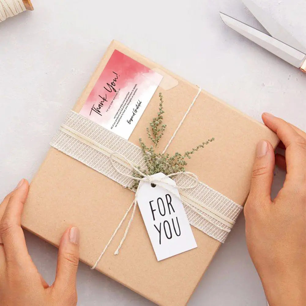 A light brown gift box tied with natural twine and a thank you tag is held by hands.