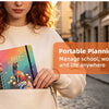 A woman holds an orange A5 spiral bound planner with monthly tabs in a light-colored tote bag.