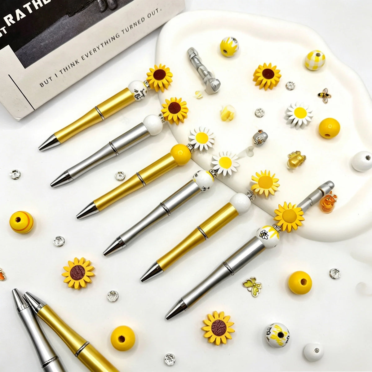 A set of gold and silver beaded pens with sunflower accents displayed on a white background.