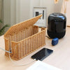 A handwoven rattan cable management box with a lid and a black cylindrical device are displayed on a wooden surface.