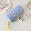 A blue and white checkered pencil case with a yellow trim is shown next to several pens and a ring.