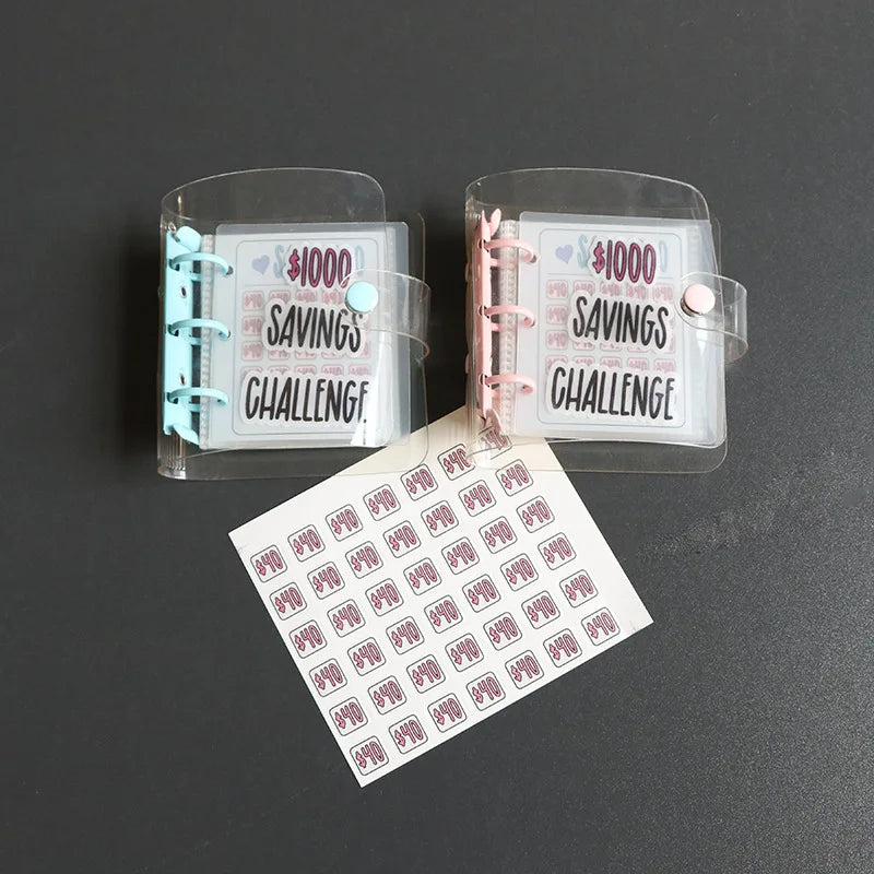 Two clear plastic binders for a savings challenge, one pink and one teal, with a sheet of savings cards in front.