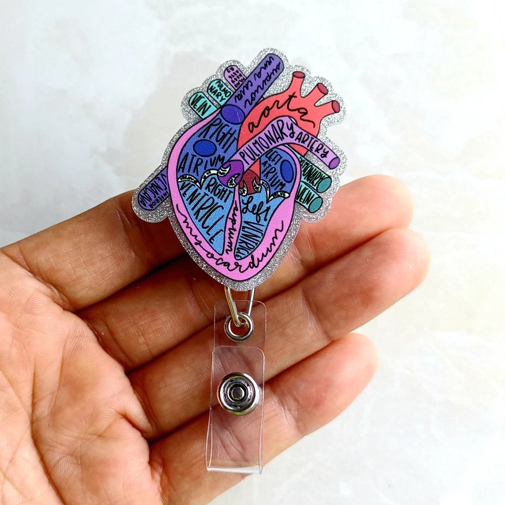 A hand holds a heart-shaped badge reel featuring an anatomical diagram of the aorta and pulmonary arteries.