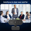 A black webcam is shown in front of a group of people in a professional meeting setting.