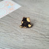 Un pequeño pin de esmalte de color dorado con forma de un gato negro y amarillo adorable, descansando sobre una superficie de