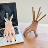 A hand-shaped decoration made of pink resin palm with wooden sticks inside, resting on a laptop.