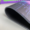 A close-up view of a black gaming mouse pad featuring a subtle purple and blue samurai design.