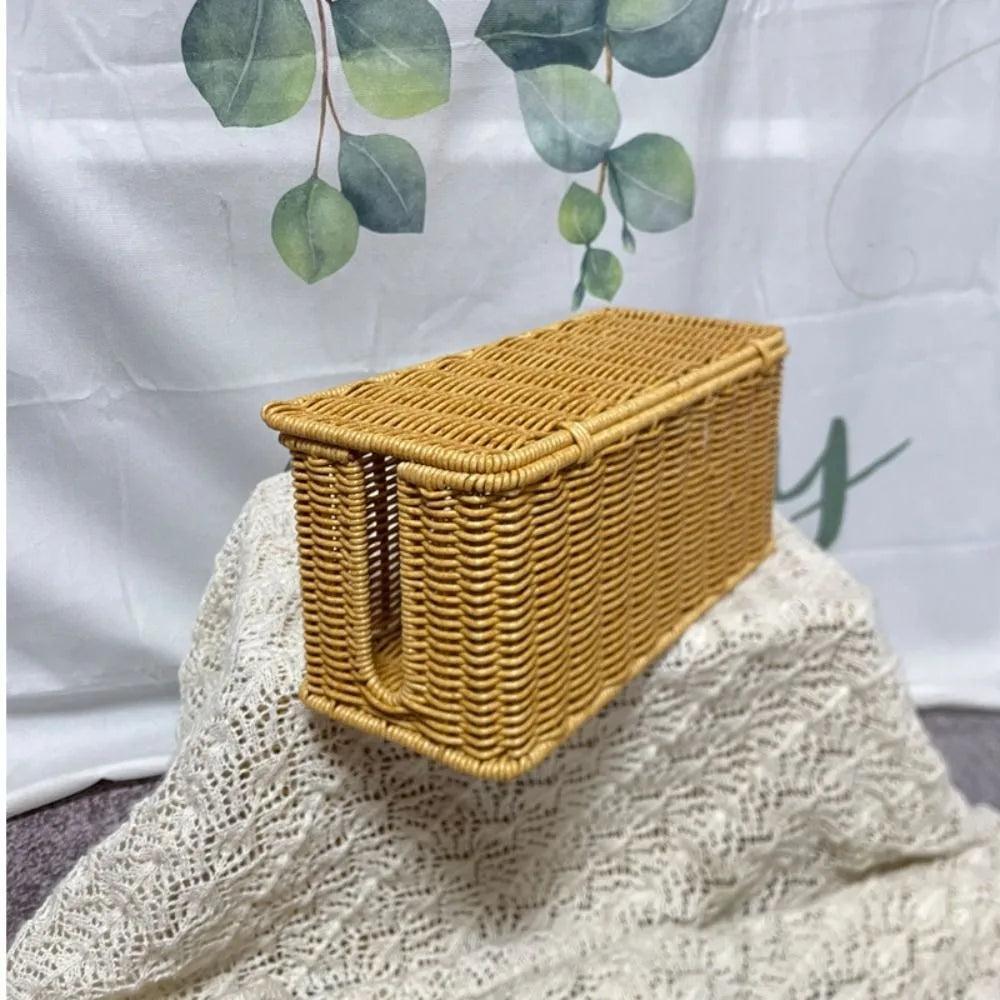 A rectangular handwoven rattan cable management box with a lid resting on a white crocheted fabric.
