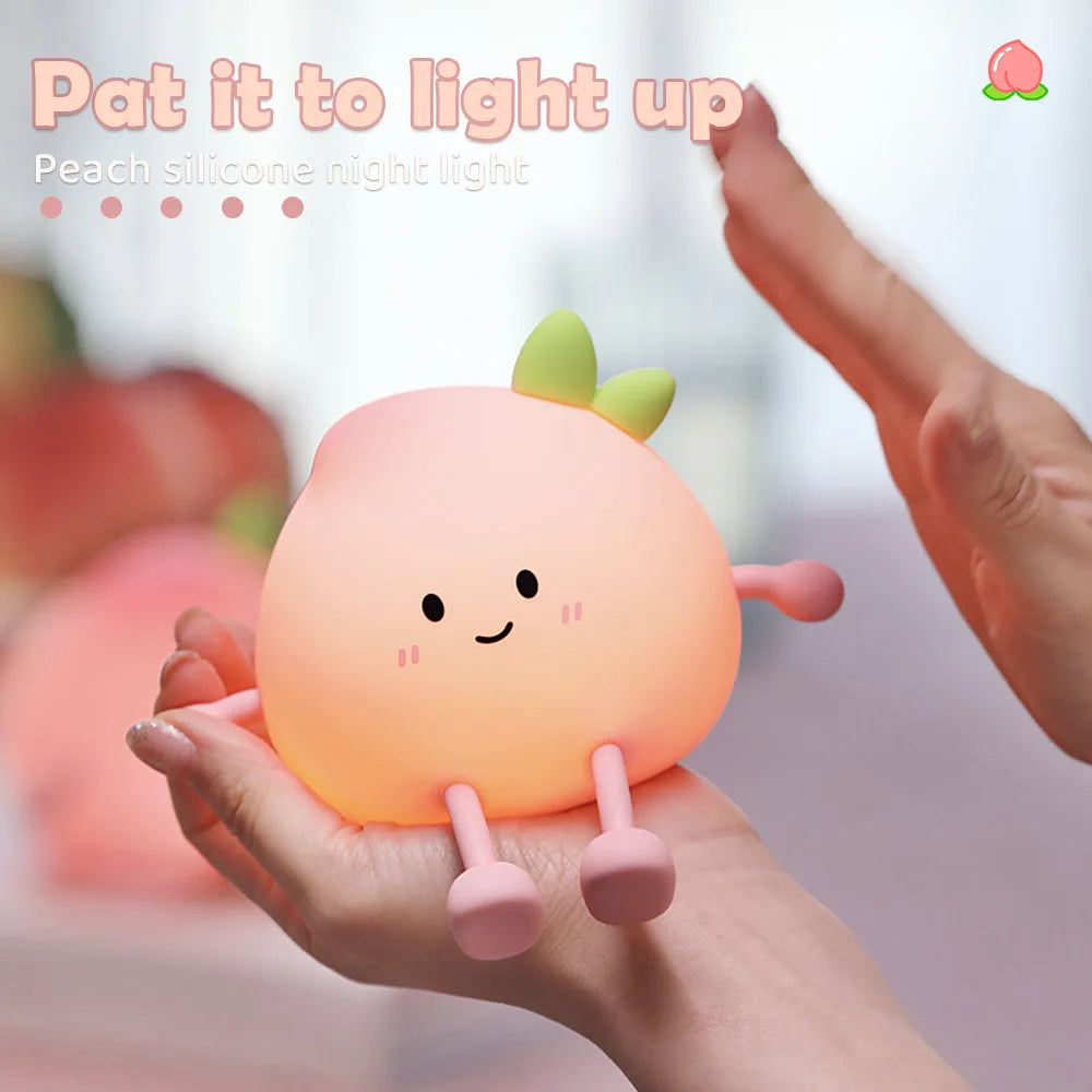 A hand holds a soft, peach-shaped silicone night light with green accents, illuminating a cute face.
