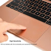 A hand is touching the smooth, rose gold trackpad area of a laptop, demonstrating high sensitivity.