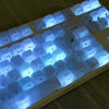 Close-up view of custom profile keycaps for a mechanical keyboard showing various letter and number keys illuminated with blu