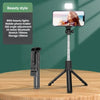 A black selfie stick tripod with an LED light and Bluetooth remote is shown on a wooden table.