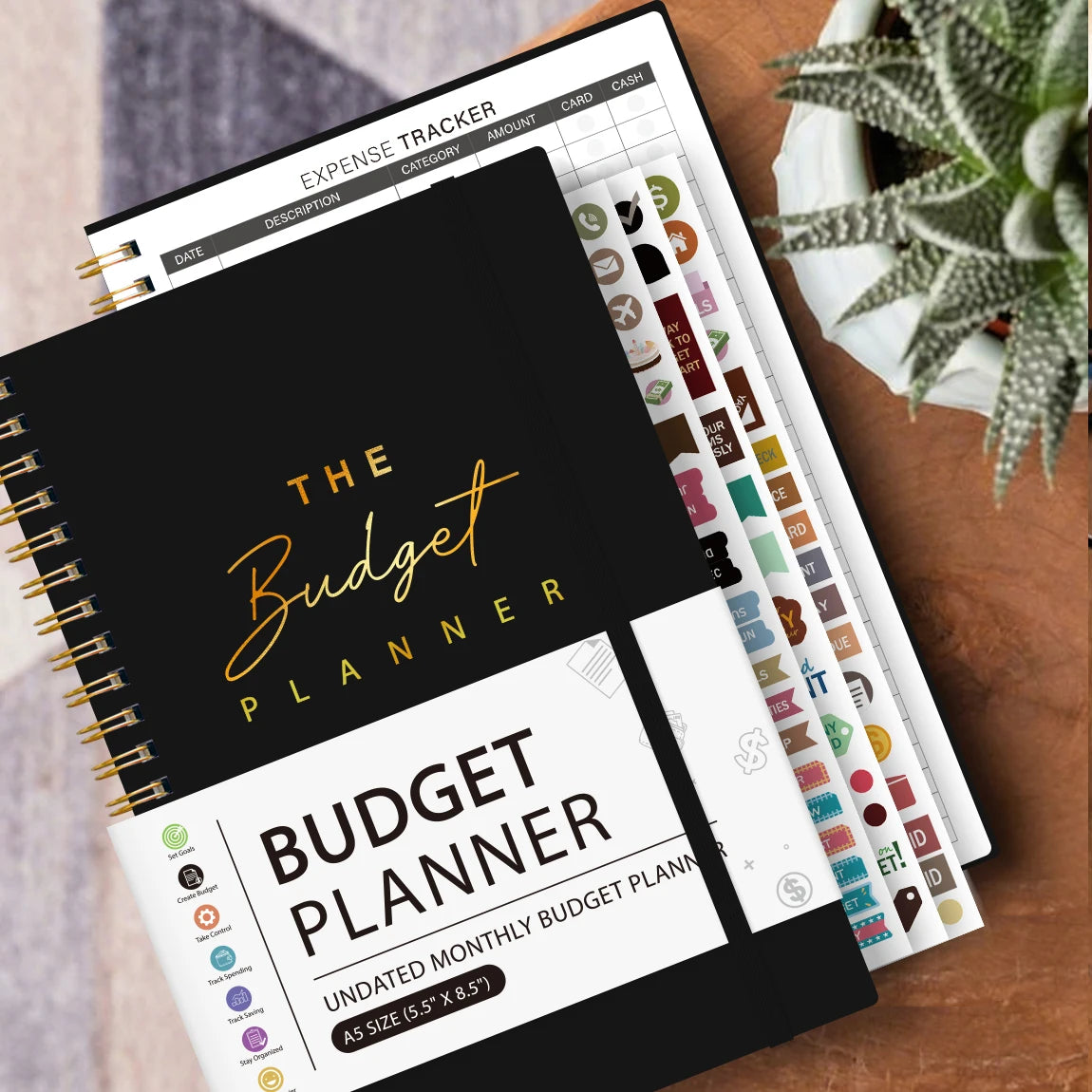 A black and gold budget planner notebook with monthly budget planning pages resting on a wooden surface.
