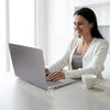 Une femme travaille sur un ordinateur portable avec un cardigan blanc et une tasse blanche sur un bureau en bois clair.