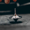 A silver metal hand spinning top fidget toy resting on a dark, textured surface.