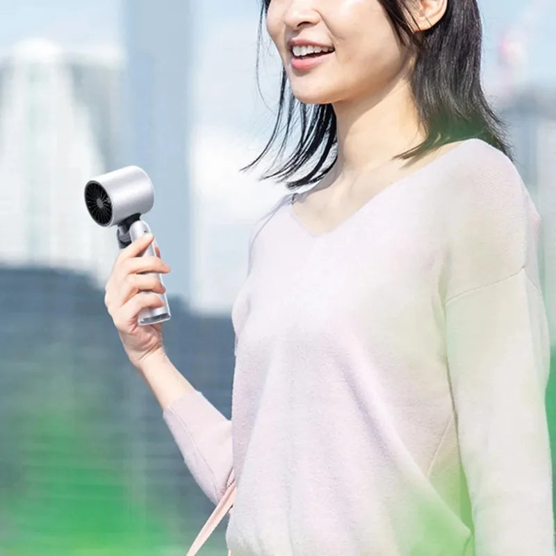 A woman holds a mini USB powered cold fan with a digital display in an outdoor setting.