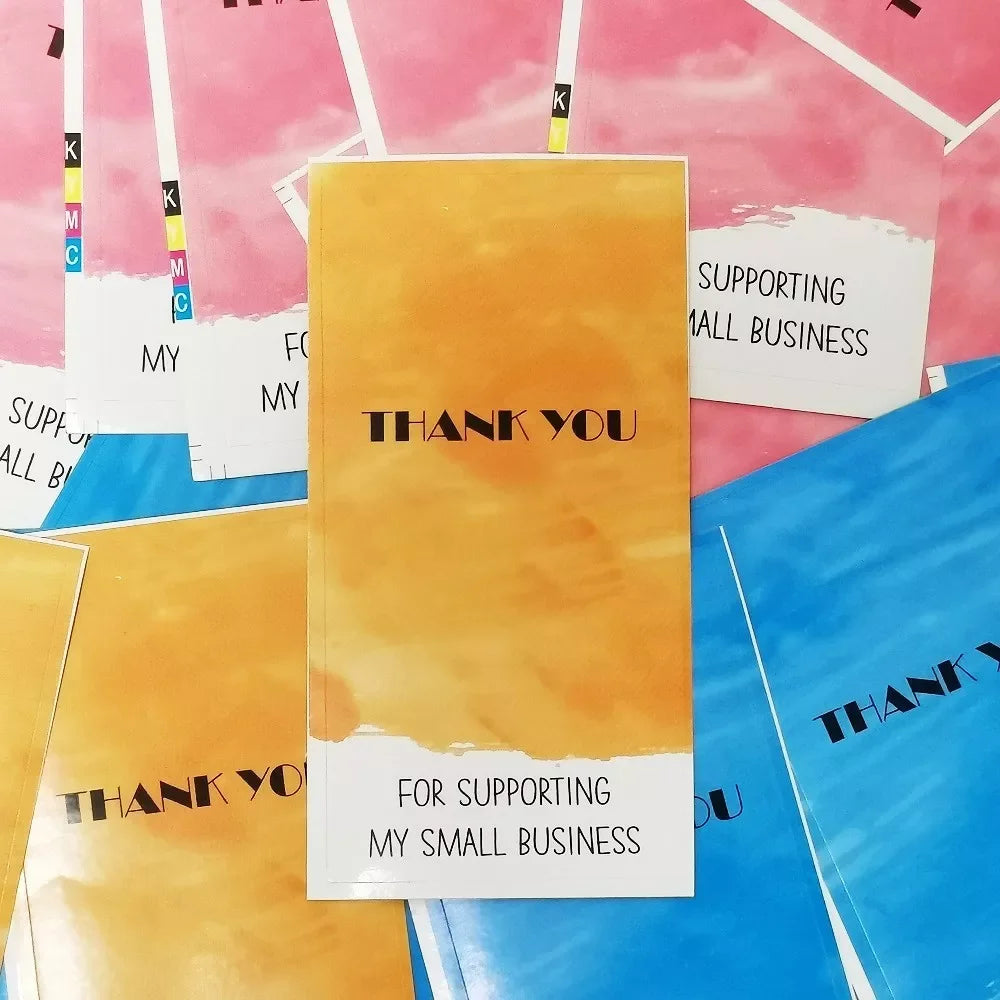 A stack of rectangular thank you gift stickers in shades of yellow, pink, and blue are displayed against a light background.