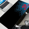 A black gaming mouse pad featuring a blue hexagonal pattern and a red dragon logo, placed next to a laptop.