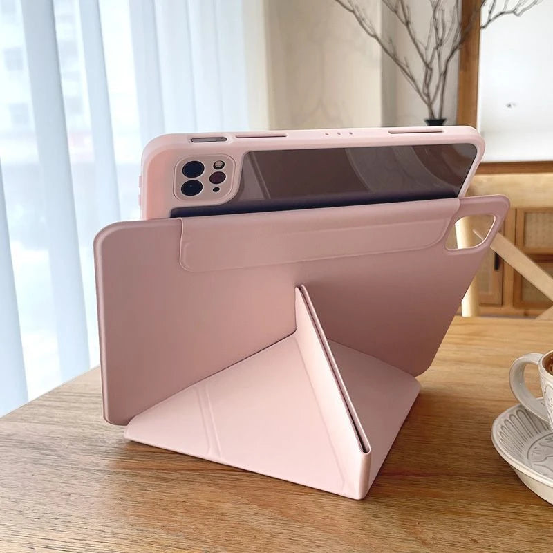 A pink magnetic protective case for an iPad, shown resting on a wooden table next to a smartphone.