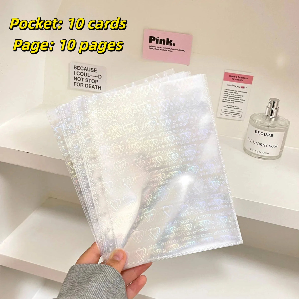 A stack of clear photo sleeves is displayed next to a pink label and a bottle of Beoupe perfume.