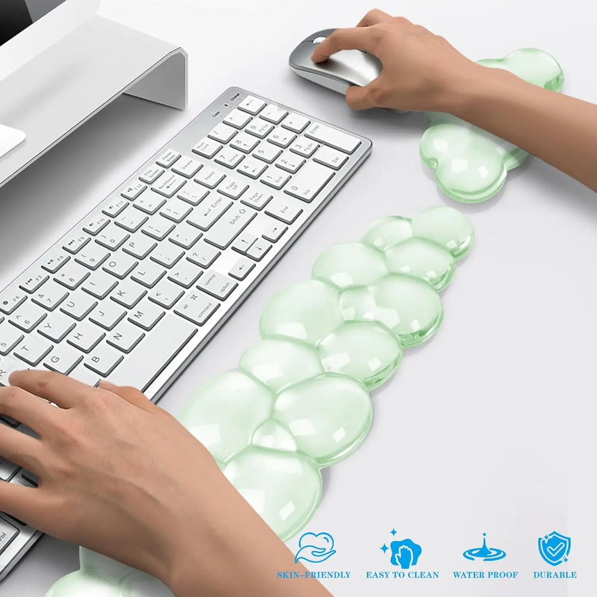 Hands place a clear, ergonomic cloud wrist rest on a white desk next to a computer keyboard.
