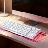 A white acrylic keyboard riser stand with an ergonomic wrist rest is placed on a light-colored desk in front of a computer mo