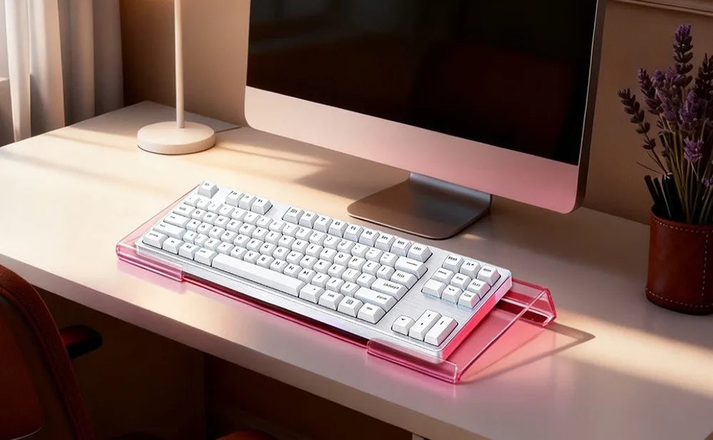 A white acrylic keyboard riser stand with an ergonomic wrist rest is placed on a light-colored desk in front of a computer mo