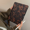 Eine Person hält eine braune Leopardenmuster-Lederhülle für ein Apple iPad und schreibt darauf mit einem weißen Stift.
