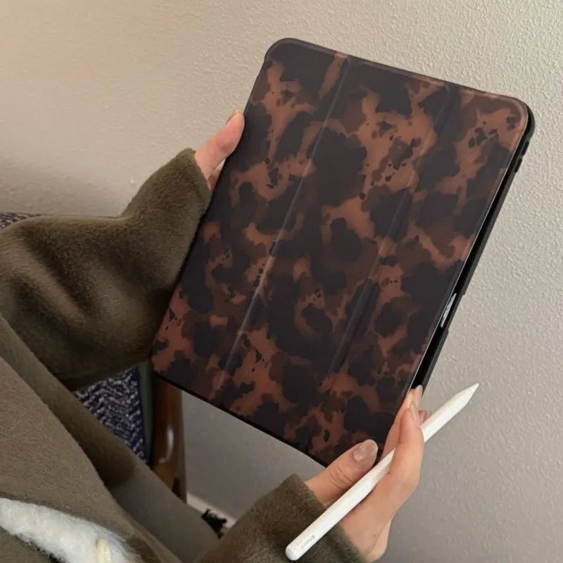 Eine Person hält eine braune Leopardenmuster-Lederhülle für ein Apple iPad und schreibt darauf mit einem weißen Stift.