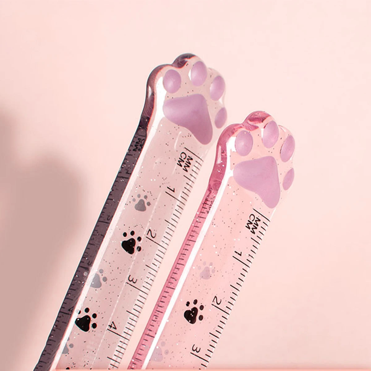 A pink plastic measuring tool shaped like a cat paw, used for measuring, with paw prints marked on the scale.