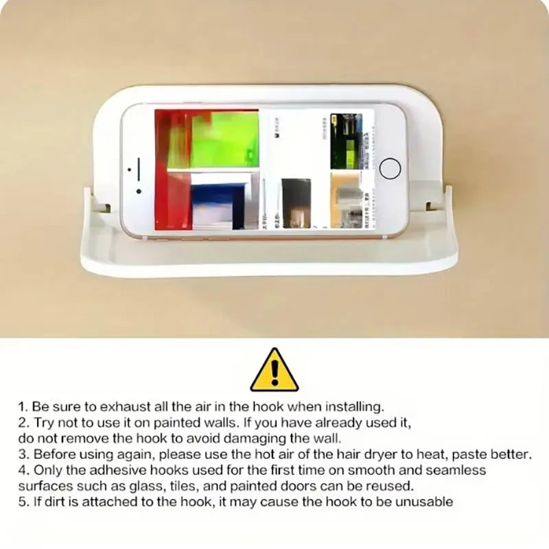A white foldable wall shelf hook with a smartphone mounted on it, shown against a beige background.
