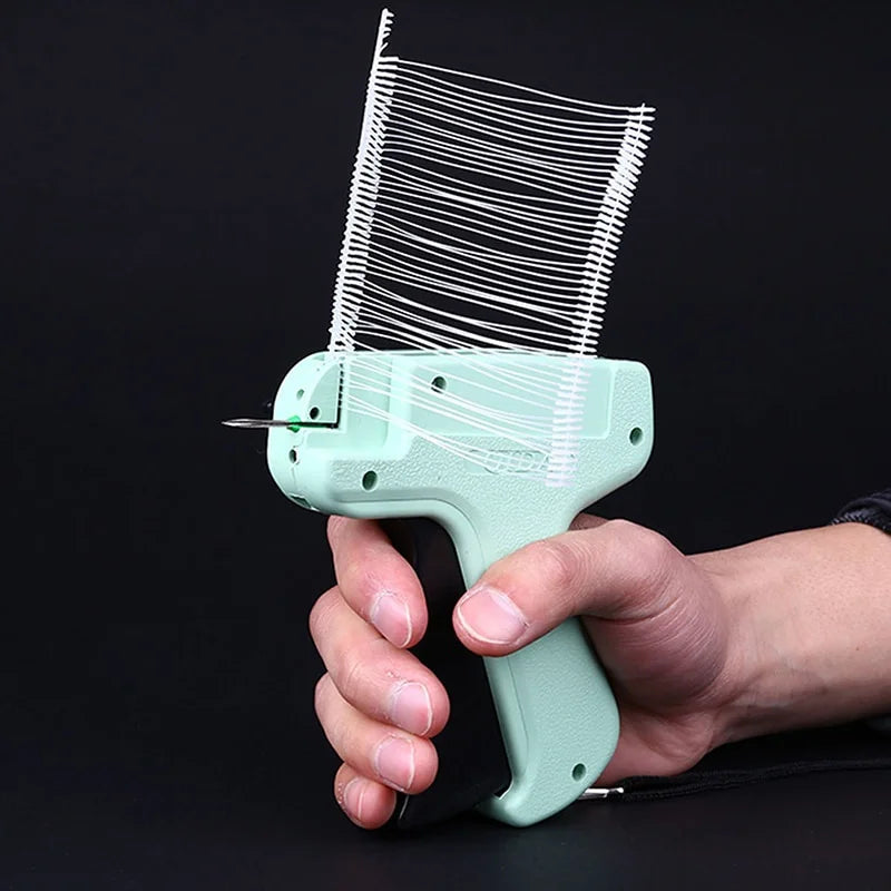 A hand holds a light green apparel tagging gun kit with a fine wire tag applicator.